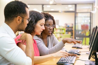 3 employees sit in front of a computer pointing at the screen.